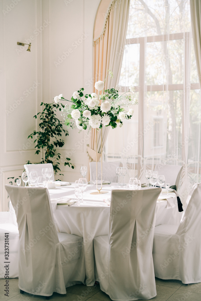 floral decoration of wedding tables, delicate white flowers and branches of fresh greenery on white hall