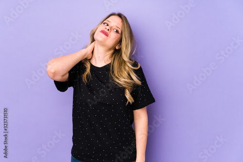 Young caucasian woman isolated on purple background having a neck pain due to stress, massaging and touching it with hand. © Asier