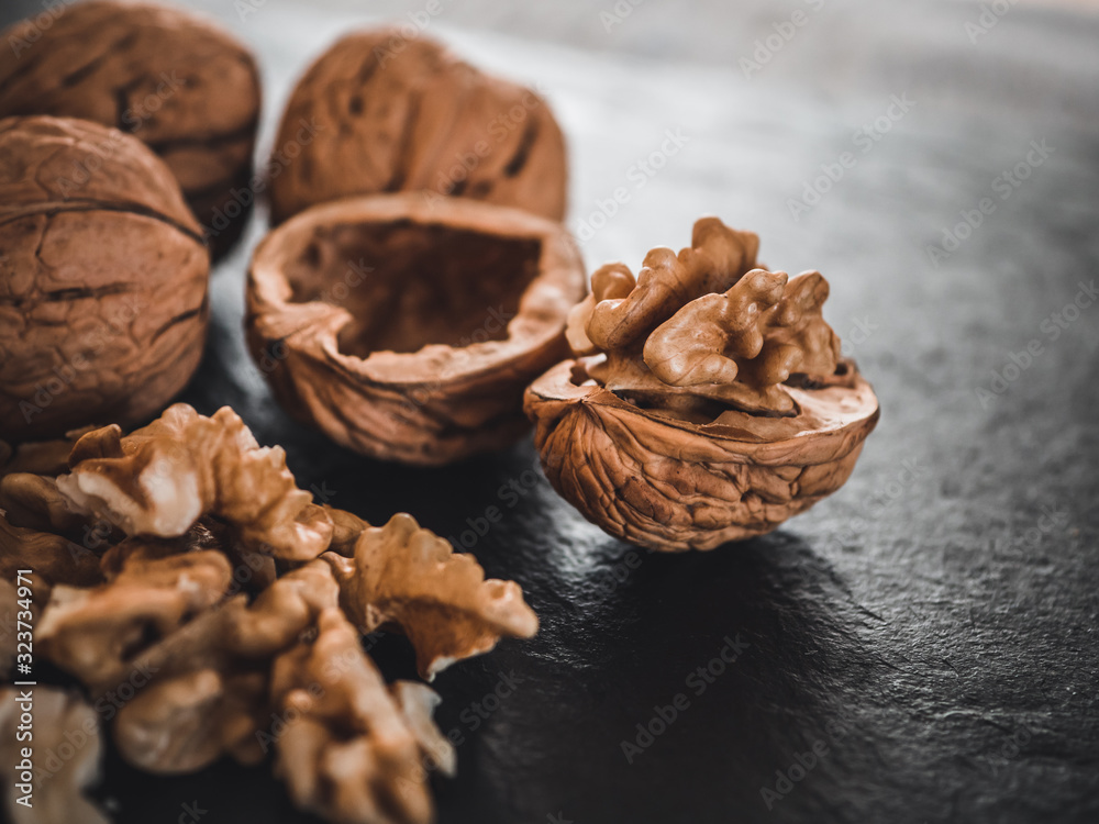 Fototapeta premium Whole walnuts on dark board. Walnut kernels on dark background. Healthy food nuts.