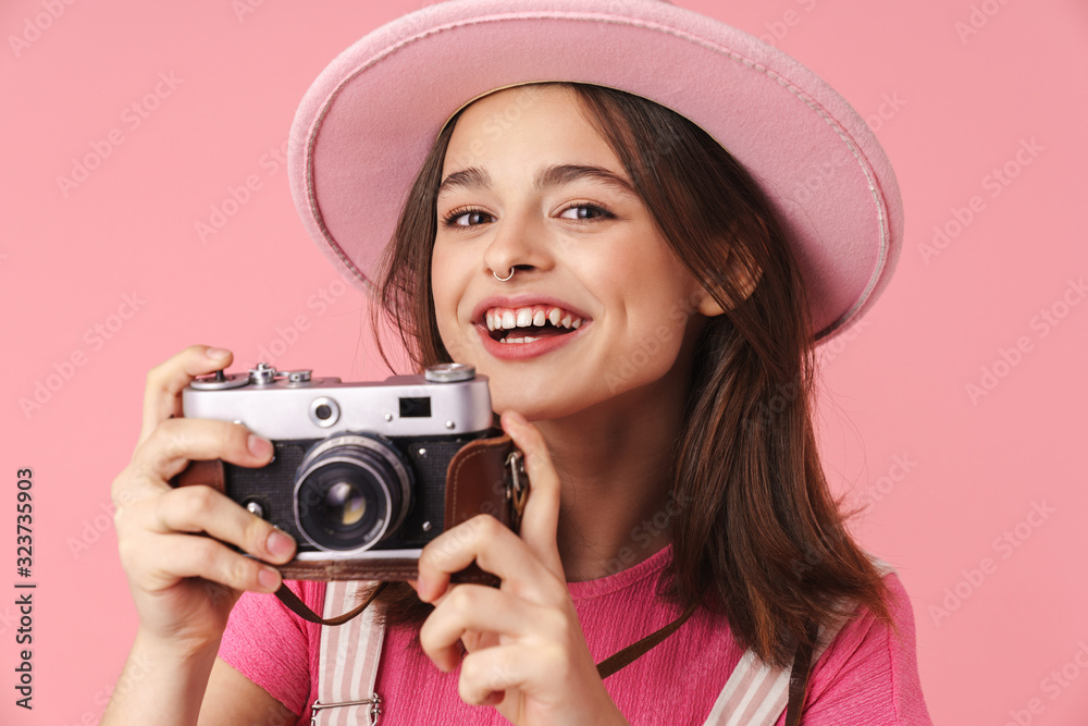 Photo of lovely charming girl in hat smiling and using retro camera