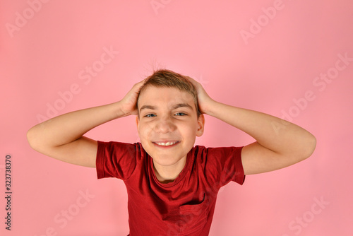 Funny boy in a burgundy T-shirt holds his head with his hands on a pink background, wide angle photo with geometric distortions.