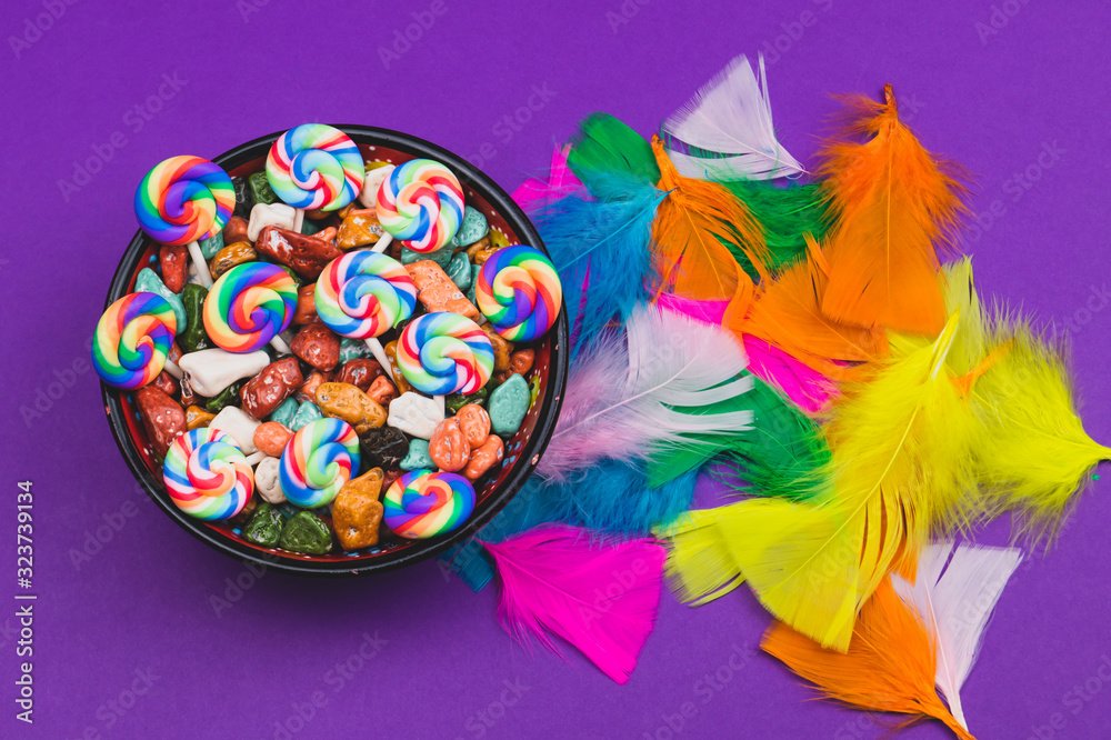 Obraz premium Candy pebbles in a bowl and lollipops. spiral candies and sweets in the form of colored stones. colorful feathers