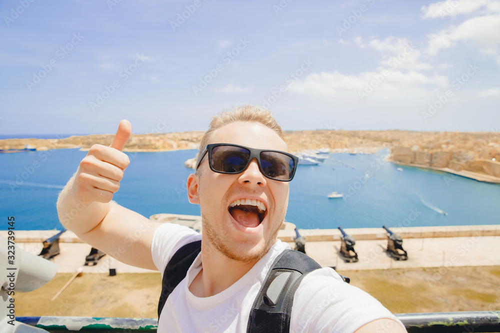 Valletta Malta happy tourist man in glasses makes selfie photo on background panorama gun bay