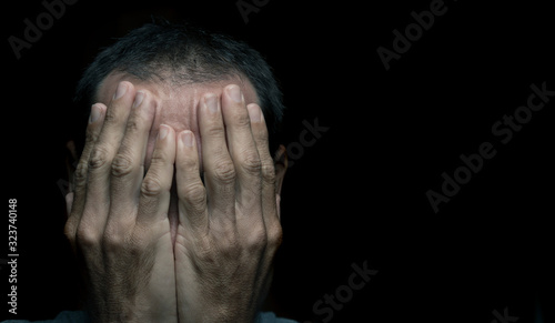 guilty or ashamed  young  man hiding his face  with hand in black background  photo