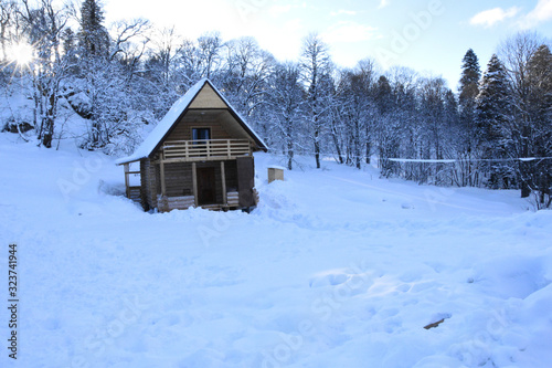 A small two-story wooden house stands in the forest, and there is snow all around. Winter fairy tale lonely chalet house.