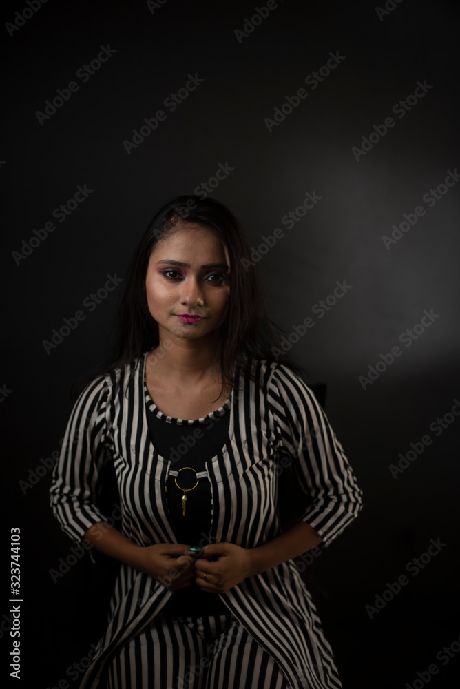 Fashion portrait of an young and attractive Indian Bengali brunette girl with striped western semi formal/casual dress in front of a black studio background. Indian fashion portrait and lifestyle.