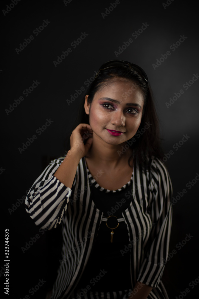 Fashion portrait of an young and attractive Indian Bengali brunette girl with striped western semi formal/casual dress in front of a black studio background. Indian fashion portrait and lifestyle. Fashion portrait of an young and attractive Indian Bengali brunette girl with striped western semi formal/casual dress in front of a black studio background. Indian fashion portrait and lifestyle.