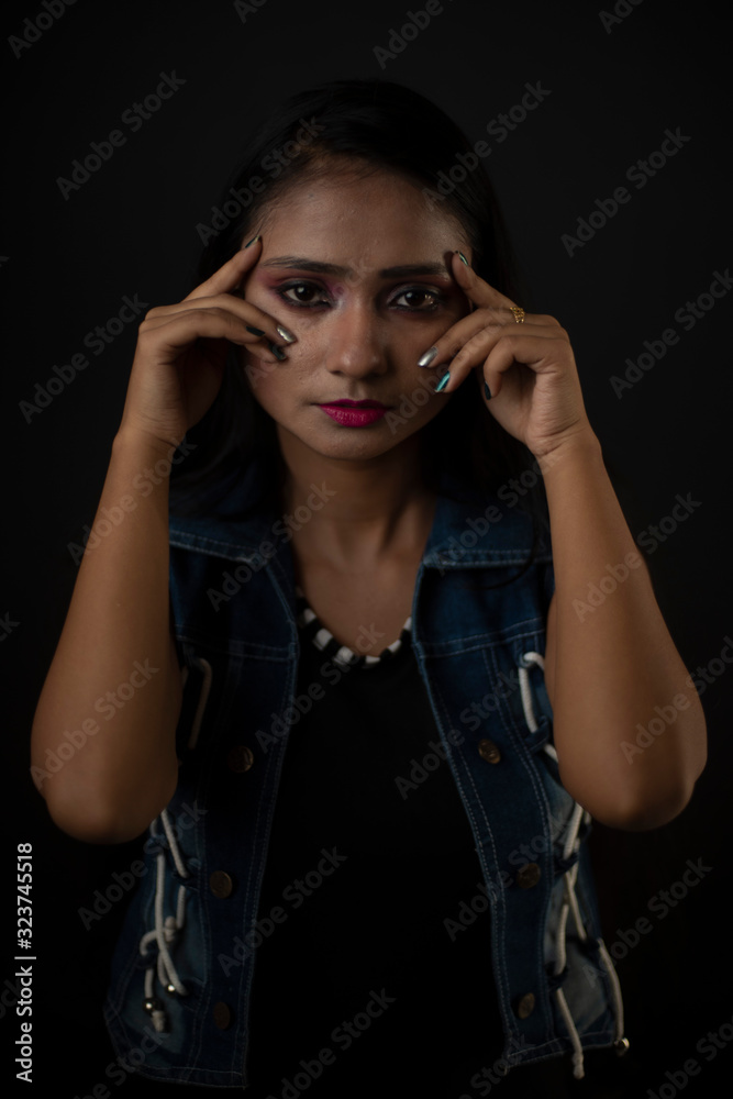 Fashion portrait of an young and attractive Indian Bengali brunette girl with tee shirt and blue western jacket tying hair in front of a black studio background. Indian fashion portrait and lifestyle. Fashion portrait of an young and attractive Indian Bengali brunette girl with tee shirt and blue western jacket tying hair in front of a black studio background. Indian fashion portrait and lifestyle.