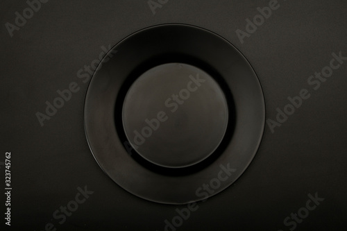 Black ceramic plate mock up for design isolated on black background, close-up top view. Copy space.