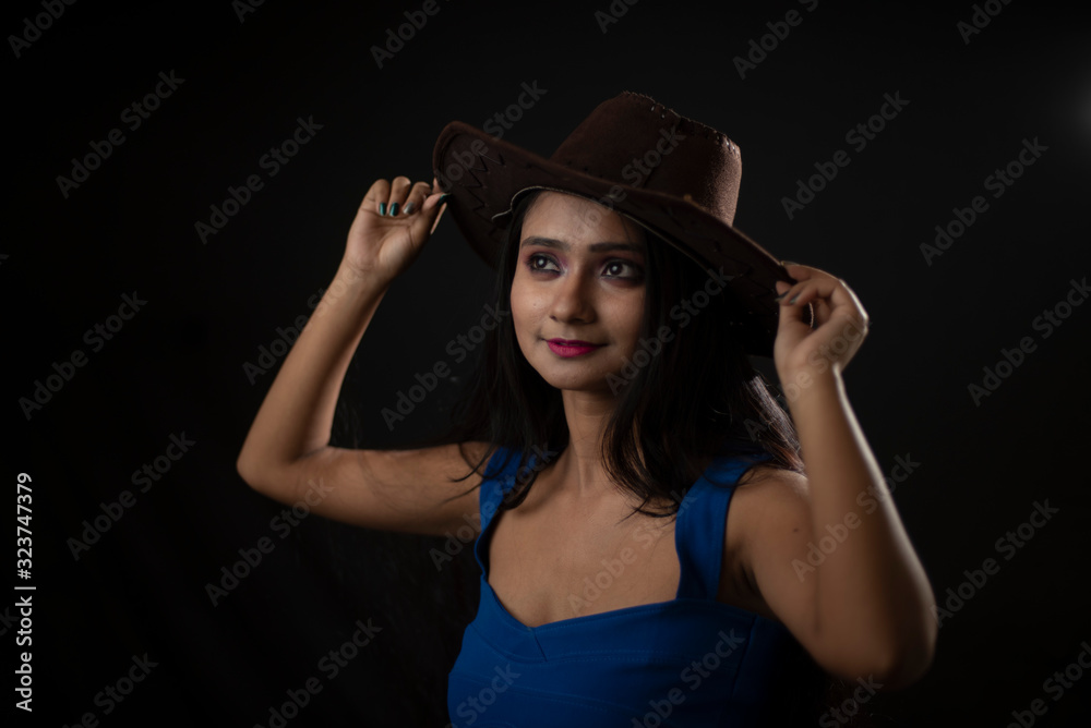 Fashion portrait of young and attractive Indian Bengali brunette girl with blue western dress with cowboy hat under spotlight in front of black studio background.Indian fashion portrait and lifestyle. Fashion portrait of young and attractive Indian Bengali brunette girl with blue western dress with cowboy hat under spotlight in front of black studio background.Indian fashion portrait and lifestyle.