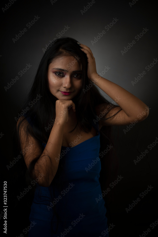 Fashion portrait of an young and attractive Indian Bengali brunette girl with blue western dress in front of a black studio background. Indian fashion portrait and lifestyle. Fashion portrait of an young and attractive Indian Bengali brunette girl with blue western dress in front of a black studio background. Indian fashion portrait and lifestyle.