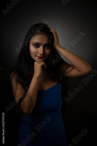 Fashion portrait of an young and attractive Indian Bengali brunette girl with blue western dress in front of a black studio background. Indian fashion portrait and lifestyle. © abir