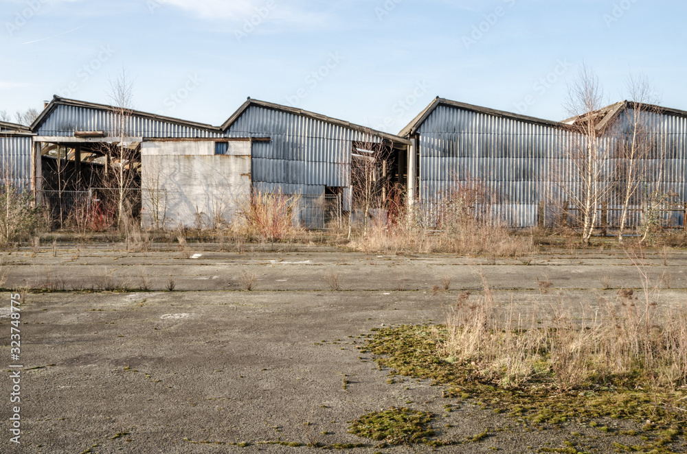Row of dilapidated factory buildings slowly overgrown with nature.