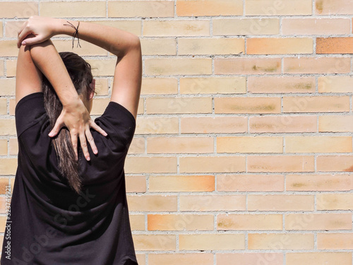 Mujer joven haciendo yoga con camisa negra y fondo de ladrillo