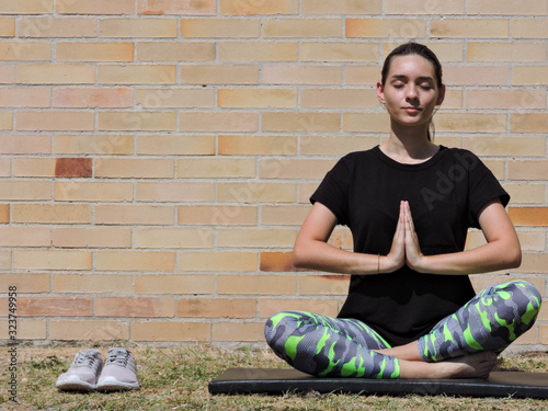 Mujer joven haciendo yoga con camisa negra y fondo de ladrillo
