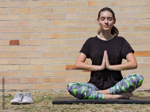 Mujer joven haciendo yoga con camisa negra y fondo de ladrillo