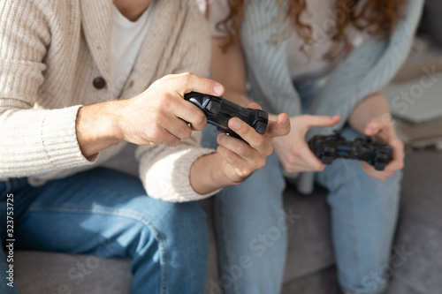 Close-up of unrecognizable friends in casual clothing using joysticks while having fun with video game