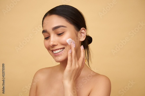 Young girl smiles and puts cream on her face on a yellow background photo