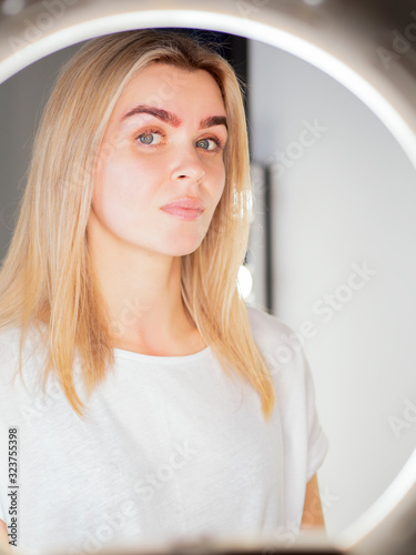 Model with angel eyes looking at camera thru the ring light lamp after microblading procedure photo