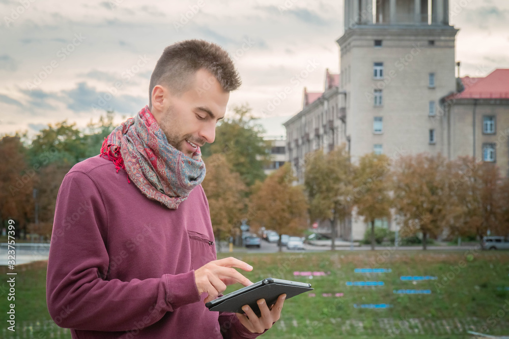Young man with tablet in hands outdoors in urban public space