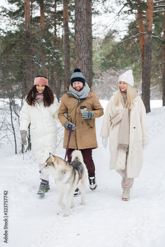 Vertical group shot of Caucasian man and two beautiful women standing with dog in urban forest on winter day
