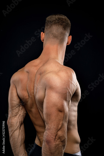 powerful muscular athlete shows off his back beside black wall