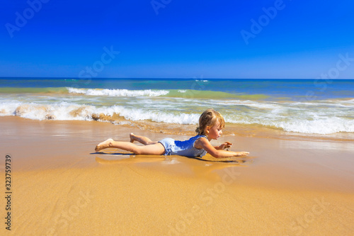Happy child lies on the sand and has fun