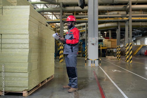 Horizontal full shot of Black male factory worker counting quantity of heat-insulating slabs