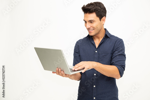 Portrait of an excited man holding laptop computer and celebrating success over white background, Raising arms with a look of happiness, Male model