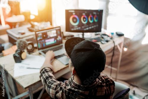 Behind Content creator man working with gear in the house studio, he is editing video footage online content job of freelance and laptop, camera photo