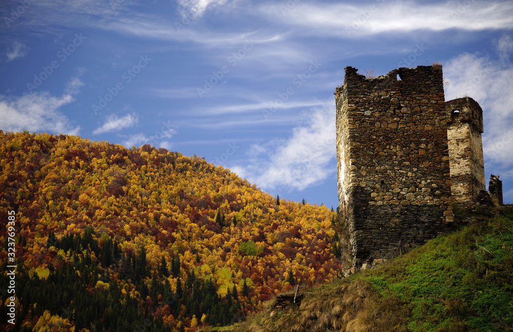 Beautiful view of old brick tower of Svaneti in colorful forest with autumn leaves and bright blue sky, Georgia