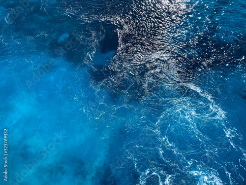 Natural blue background. Blue surface of sea water with wave and foam. Texture of blue water. Abstract textured backdrop. Horizontal, blur, cropped shot, free space for text. Concept of natural beauty