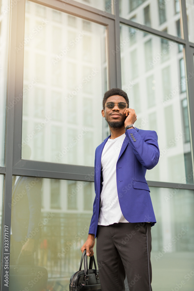 handsome young african man in a suit with a phone in his hands near a glass building handsome young african man in a suit with a phone in his hands near a glass building