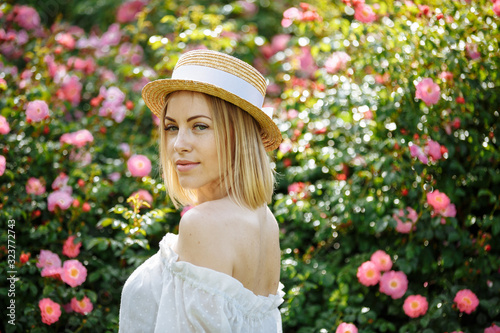 girl in a white dress with a hat in the garden with pink roses