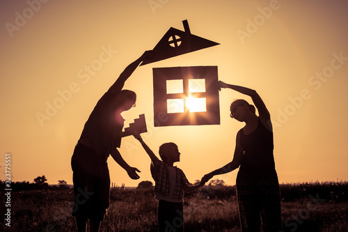 Happy family standing on the field at the sunset time. They build a house.