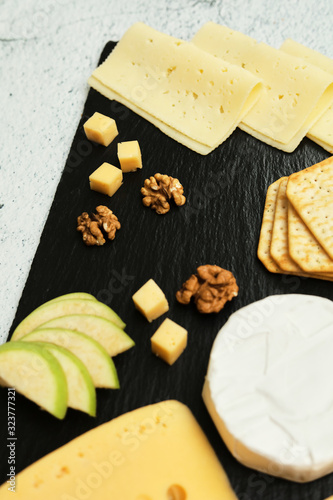 Pieces of cheese on a dark background. Cheeseboard. Sliced ​​apple and nuts on the board. Hard cheese, camembert, roquefort, emmental.