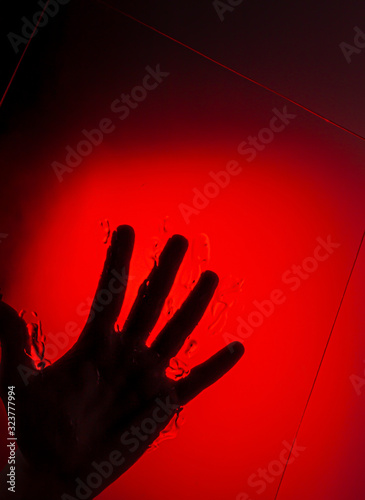 human hand on glass on red background, in dark. Symvol reflection. photo