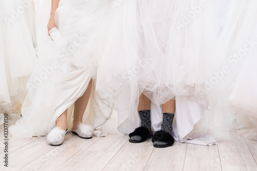 Horizontal shot of two funny unrecognizable women wearing wedding dresses and slippers