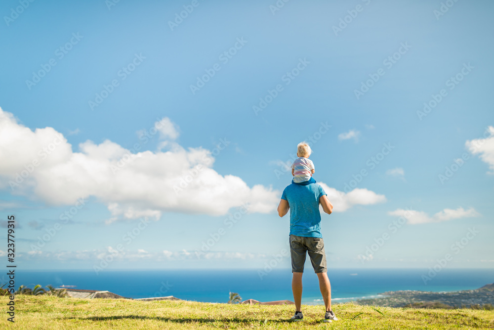 Happy father giving son piggyback outdoors looking at the beautiful ocean view. Parenting and spending time with your children concept. 