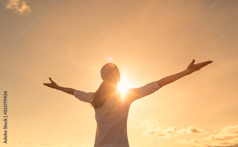 Happy positive woman looking up to the sunset sky with arms up feeling free