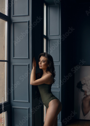 Young sexy girl in green bodysuit poses near the window.