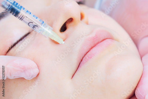 Close-up Of Beautician Injecting Botox On Female Lips. She holds a syringe. Young beautiful woman gets procedure with pleasure