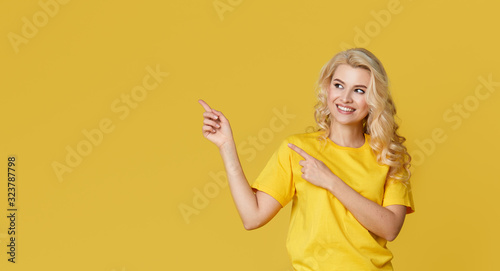 Young happy woman shows hands up, spreads his hands to the sides. Above is an empty place for text and inscription on a yellow background.