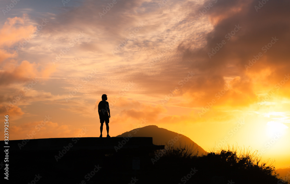 Young man standing on a hill watching the morning sunrise 