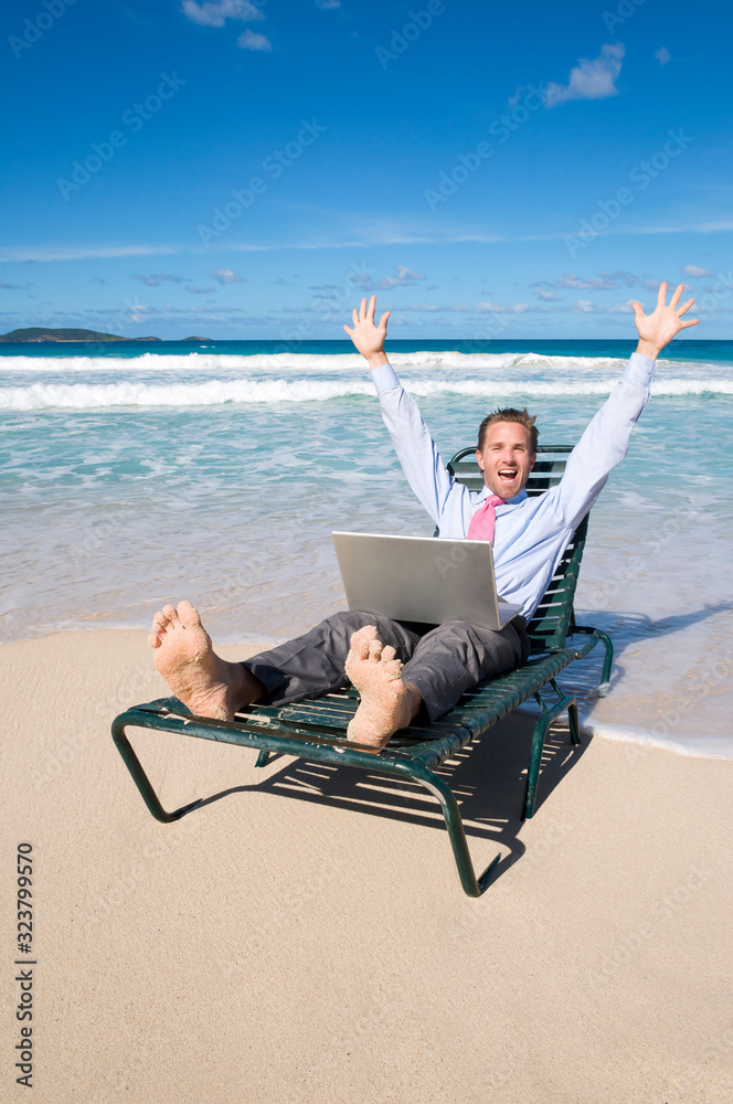 Excited barefoot businessman celebrating outdoors with his computer on a tropical beach