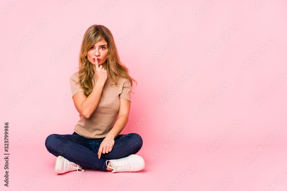 Young blonde caucasian woman sitting on a pink studio keeping a secret or asking for silence. Young blonde caucasian woman sitting on a pink studio keeping a secret or asking for silence.