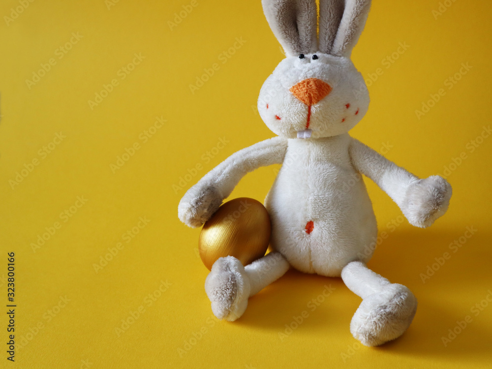Gold Easter egg with a rabbit toy on colorful yellow background. Happy Easter concept, copy space. Gold Easter egg with a rabbit toy on colorful yellow background. Happy Easter concept, copy space.