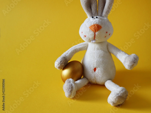 Gold Easter egg with a rabbit toy on colorful yellow background. Happy Easter concept, copy space. © Zhanna