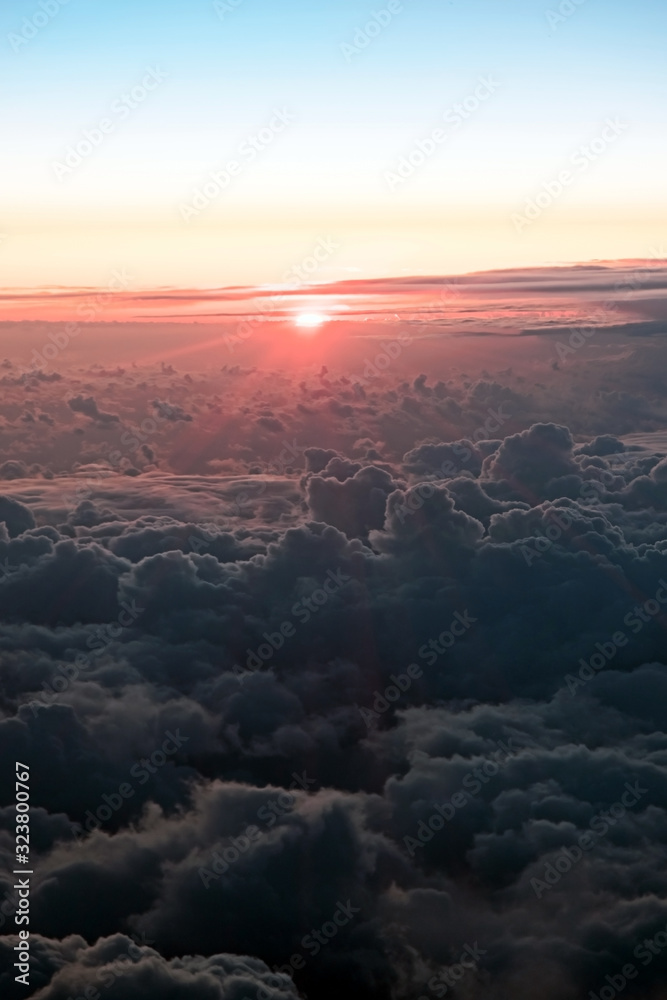 Sunset above clouds illuminated by the rays of the sun from airplane window. View of the beautiful cumulus clouds at sunset from an airplane window, true colors.