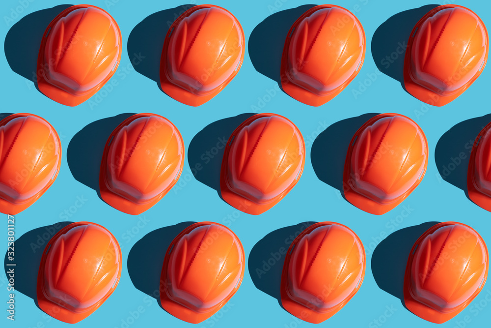 © Andrii - orange safety helmet rows on a blue background with hard shadows. looking from above.industrial pattern backdrop.